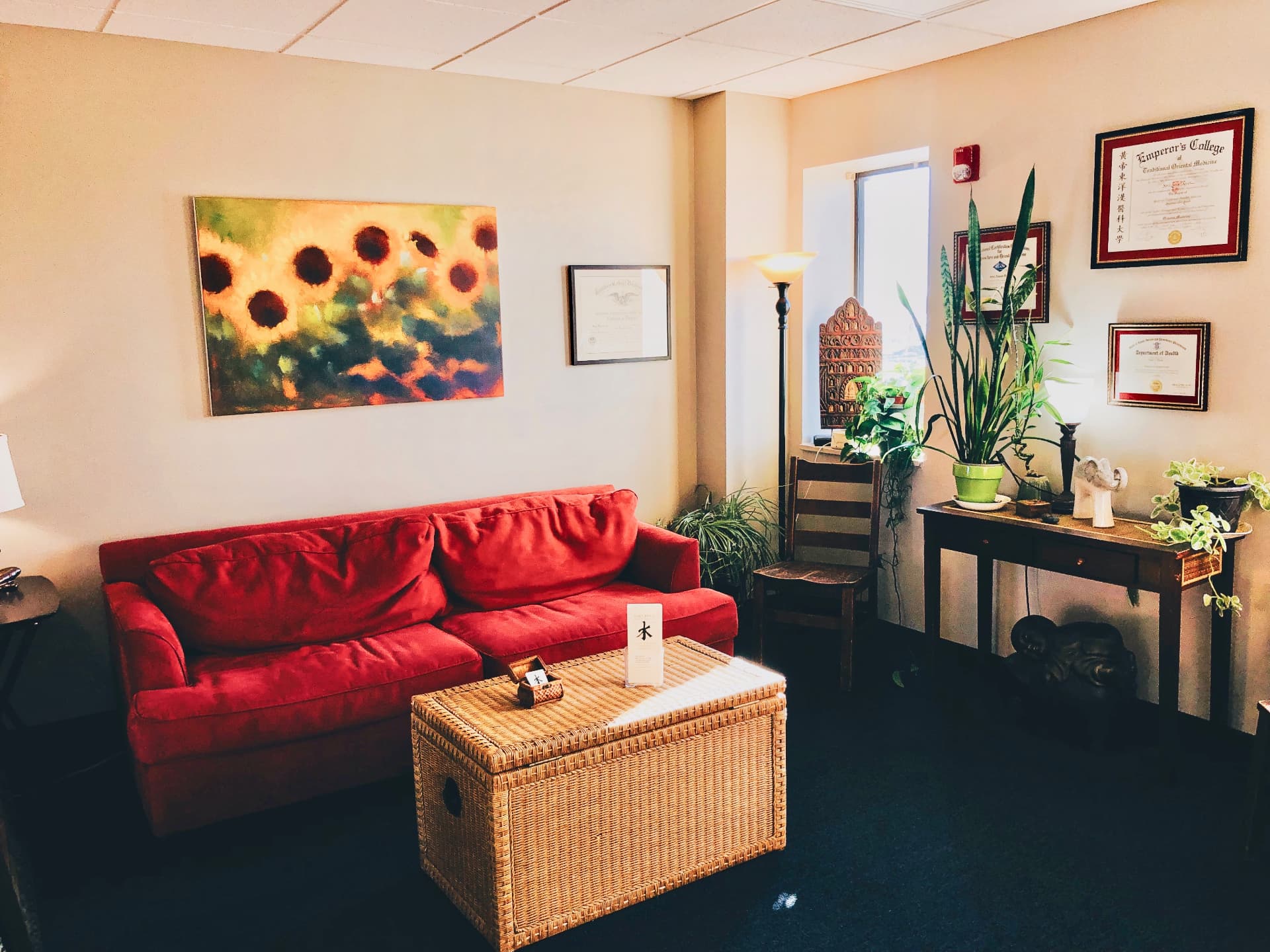 Waiting area with red couch, sunflower painting, and framed diplomas